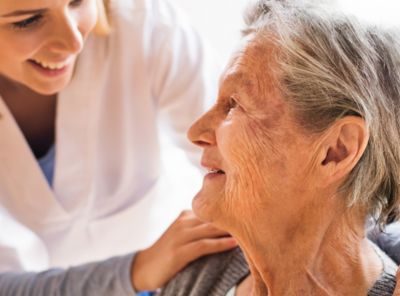 afbeelding van zorgprofessional die zich vriendelijk buigt naar een oudere patiënte