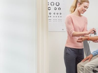 Afbeelding van een huisarts met een stethoscoop die bij een patiënt de bloeddruk opneemt