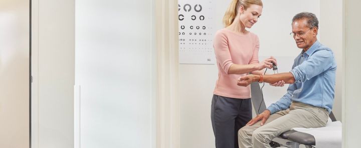 persbericht Afbeelding van een huisarts met een stethoscoop die bij een patiƫnt de bloeddruk opneemt